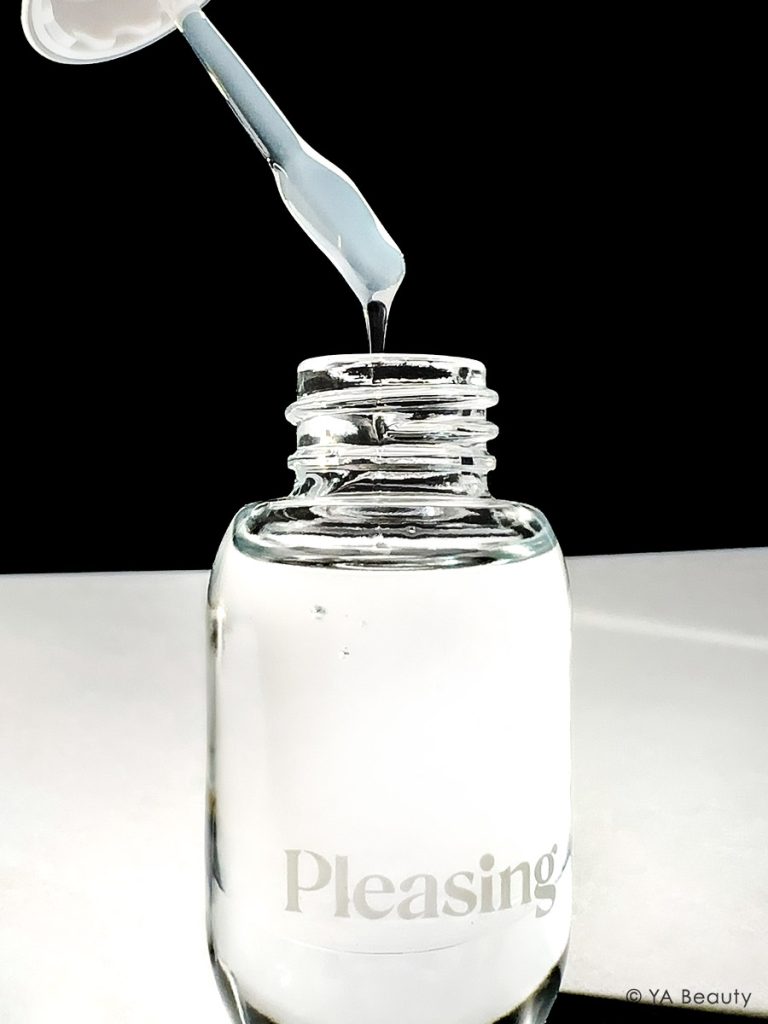The Pleasing by Harry Styles x Marco Ribeiro collaboration product Gloss Medium. The cap and spatula is held in the air as the gloss drips back down into the clear, glass bottle. Striking editorial photography on black and white background